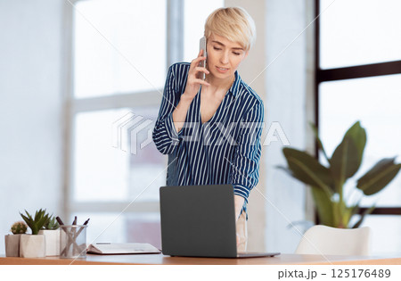 Business Lifestyle. Businesswoman Talking On Cellphone Standing Near Workdesk In Modern Office. Selective Focus, Empty Space Business Lifestyle. Businesswoman Talking On Cellphone Standing Near Workdesk In Modern Office. Selective Focus, Empty Space 125176489