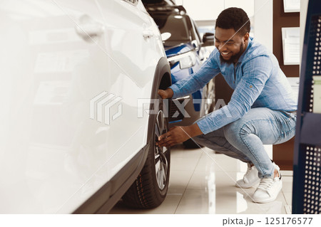 Choosing Car. Afro Guy Checking Wheels Buying Auto In Dealership Store. Copy Space, Selective Focus 125176577