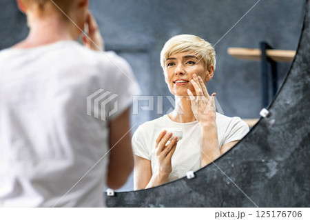 Caring For Skin. Cheerful Mature Woman Applying Facial Cream Preventing Aging And Wrinkles Standing In Bathroom At Home. Selective Focus 125176706