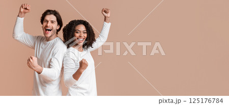 We made it. Joyful multiracial couple celebrating success, raising fists, rejoicing victory together over yellow background with free space We made it. Joyful multiracial couple celebrating success, raising fists, rejoicing victory together over yellow background with free space 125176784