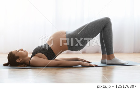 Prenatal Gymnastics. Young Pregnant Woman Training At Home, Doing Shoulder Bridge Exercise While Lying On Fitness Mat In Living Room, Expecting Lady Enjoying Healthy Lifestyle, Side View, Copy Space Prenatal Gymnastics. Young Pregnant Woman Training At Home, Doing Shoulder Bridge Exercise While Lying On Fitness Mat In Living Room, Expecting Lady Enjoying Healthy Lifestyle, Side View, Copy Space 125176807