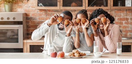 Joyful black family having fun during breakfast at kitchen, making cupcake eyes, panorama 125176833