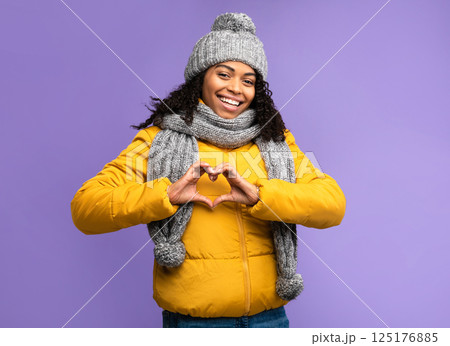 I Love Winter. Cheerful Black Woman Gesturing Heart Shape Smiling To Camera Posing Over Purple Studio Background, Wearing Warm Clothes. Love, Romance, Happy Winter Season Concept 125176885