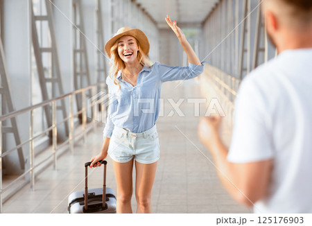 Welcome Back Home Concept. Woman waving to her man, husband meeting his wife from abroad in airport building Welcome Back Home Concept. Woman waving to her man, husband meeting his wife from abroad in airport building 125176903