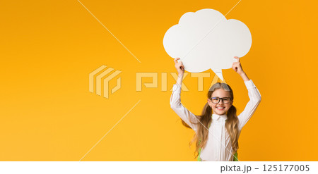 Smiling Elementary Student Girl Holding Speech Bubble Overhead On Yellow Studio Background. Thinking Of School. Mockup, Free Space Smiling Elementary Student Girl Holding Speech Bubble Overhead On Yellow Studio Background. Thinking Of School. Mockup, Free Space 125177005
