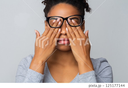 African girl in glasses rubs her eyes, suffering from tired eyes, ocular diseases concept 125177144