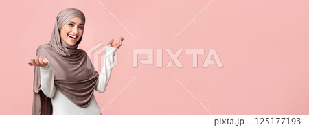 Who cares. Carefree muslim girl in hijab spreading hands and shrugging shoulders, posing over pink background, panorama with free space 125177193