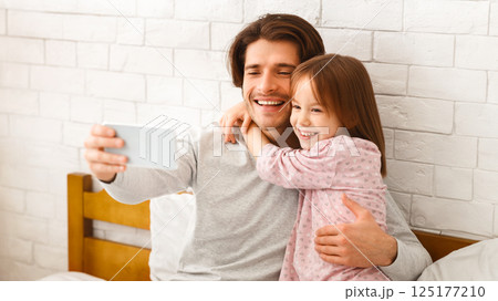 Positive hugging father and little daughter taking selfie on smartphone at home, free space Positive hugging father and little daughter taking selfie on smartphone at home, free space 125177210