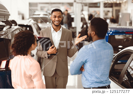 Professional Car Seller Talking With African American Couple Clients Selling Auto Working In Dealership Center. Selective Focus Professional Car Seller Talking With African American Couple Clients Selling Auto Working In Dealership Center. Selective Focus 125177277