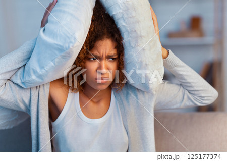 Annoyed woman covering ears with pillow, suffering from noisy neighbours Annoyed woman covering ears with pillow, suffering from noisy neighbours 125177374