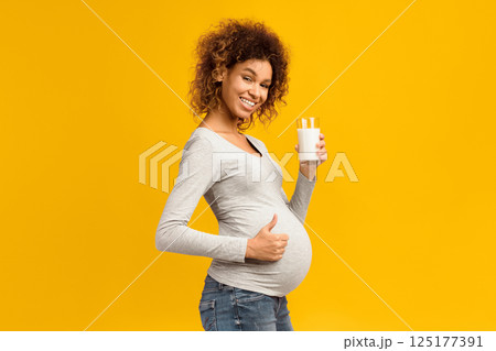 Pregnancy and calcium. Afro woman with glass of milk showing thumb up over pink studio background Pregnancy and calcium. Afro woman with glass of milk showing thumb up over pink studio background 125177391