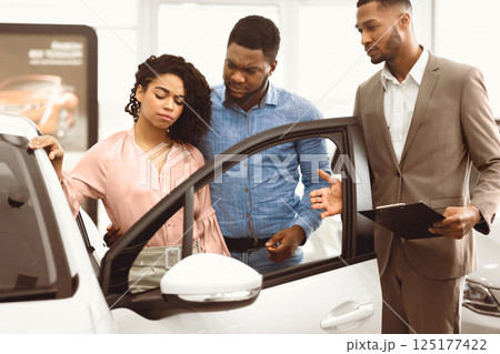 Displeased Car Buyers Looking At Auto Choosing New Automobile With Seller Man In Dealership Store. Selective Focus 125177422
