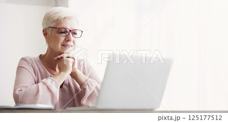 Senior excited woman reading article online, using laptop at home, free space 125177512