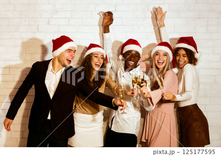 Happy New Year. Joyful Millennial Friends In Santa Hats Clinking Glasses Celebrating Christmas Winter Holidays Standing Against White Wall Indoor Happy New Year. Joyful Millennial Friends In Santa Hats Clinking Glasses Celebrating Christmas Winter Holidays Standing Against White Wall Indoor 125177595
