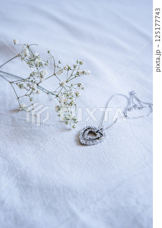 Heart-shaped pendant necklace on delicate white fabric with baby's breath floral accent 125177743