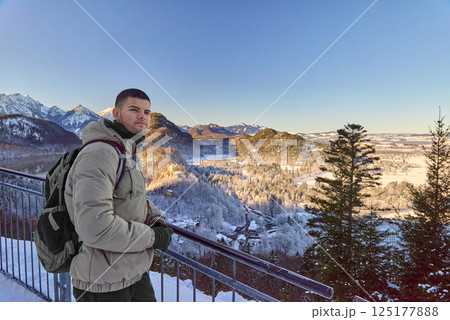 Man standing on a balcony with icy mountains and a forest in the background, breathtaking scenic view, portrait mode, winter landscape photography 125177888