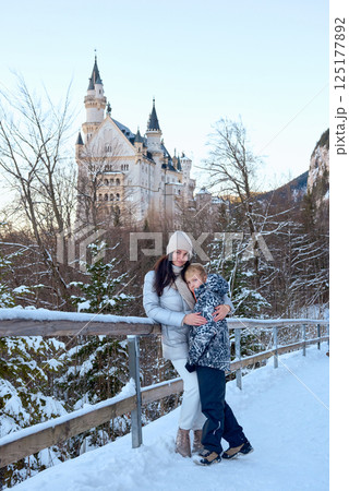 Beautiful woman and child standing on a bridge in the snow with Neuschwanstein Castle in the background, capturing a serene winter scene with a majestic castle and snowy landscape. Beautiful woman and child standing on a bridge in the snow with Neuschwanstein Castle in the background, capturing a serene winter scene with a majestic castle and snowy landscape. 125177892