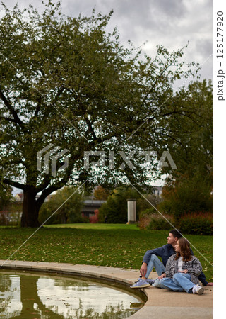 Autumn Serenity: Couple Relaxing by a Reflective Pond in an Ivy-Covered Garden with Vibrant Foliage 125177920