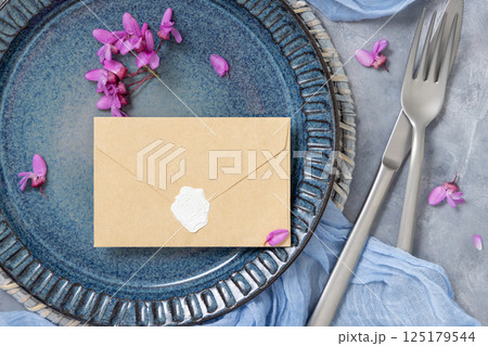 Wedding table place with sealed envelope near fabric and wild purple flowers top view, mockup 125179544