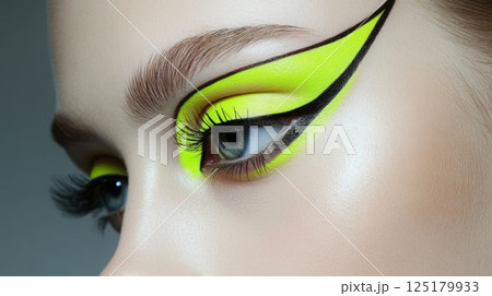 A striking close-up of eye makeup features vibrant neon yellow and black winged eyeliner accentuating the model's eyes. The artistic design highlights a creative expression in beauty. 125179933