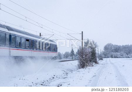 Passenger train passing through snowy fields in Germany 125180203
