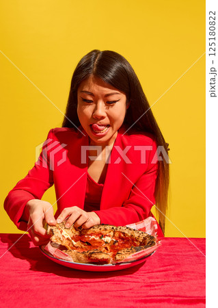Young Asian woman expressing excitement to eat delicious pizza, taking slice from plate against bright studio background. Young Asian woman expressing excitement to eat delicious pizza, taking slice from plate against bright studio background. 125180822