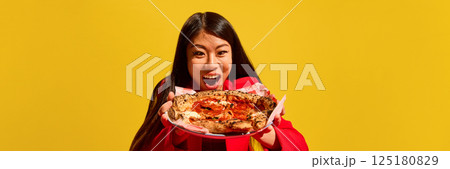 Excited Asian woman emotionally looking at plate with delicious pizza against bright yellow background. Excited Asian woman emotionally looking at plate with delicious pizza against bright yellow background. 125180829