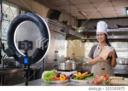 Food vlogger filming a cooking video in professional kitchen studio. Food vlogger filming a cooking video in professional kitchen studio. 125182675