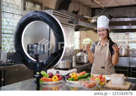 Food vlogger filming a cooking video in professional kitchen studio. 125182678