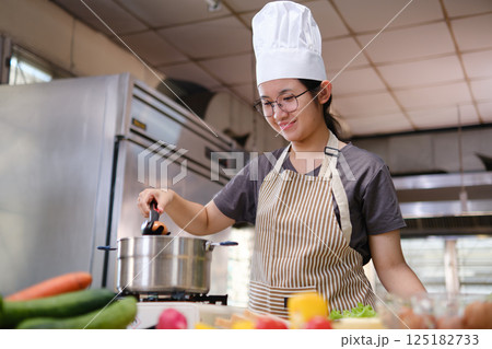 Young chef boiling eggs in a modern kitchen surrounded by fresh vegetables and sandwich ingredients. 125182733