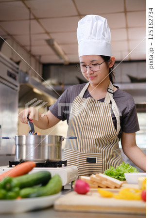 Young chef boiling eggs in a modern kitchen surrounded by fresh vegetables and sandwich ingredients. 125182734