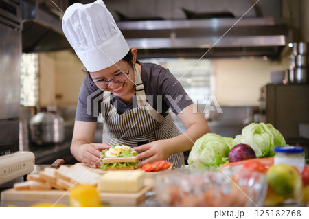 Focused chef carefully a gourmet sandwich in a professional kitchen with fresh ingredients in view 125182768