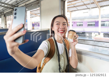 Selfie and Coffee Break. A cheerful traveler taking a selfie while savoring a warm drink in a train carriage. Selfie and Coffee Break. A cheerful traveler taking a selfie while savoring a warm drink in a train carriage. 125182911