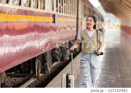Travel and Adventure. A young woman walking with a suitcase towards a train station. Travel and Adventure. A young woman walking with a suitcase towards a train station. 125182981