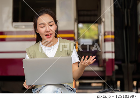 Traveling and Video Call Engagement. A young woman animatedly converses over her laptop while waiting at a train station. 125182997
