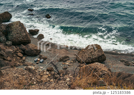 Rugged shoreline with rocky beach and gentle waves crashing on a calm afternoon 125183386
