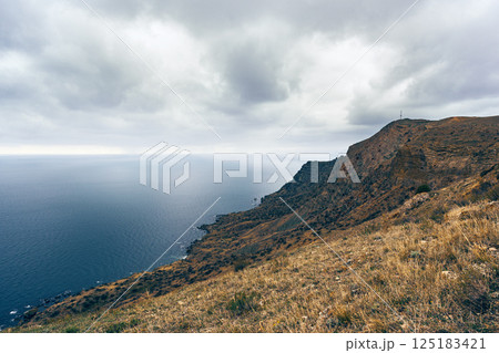 Coastal panorama with rocky cliffs and moody sky near the ocean during late afternoon 125183421