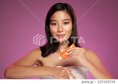 Model applying skincare product against a vibrant purple background during a photoshoot in a studio setting Model applying skincare product against a vibrant purple background during a photoshoot in a studio setting 125183534
