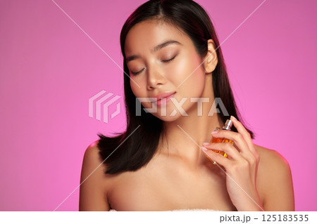 Woman enjoying perfume with closed eyes in a vibrant pink background during a beauty photoshoot Woman enjoying perfume with closed eyes in a vibrant pink background during a beauty photoshoot 125183535