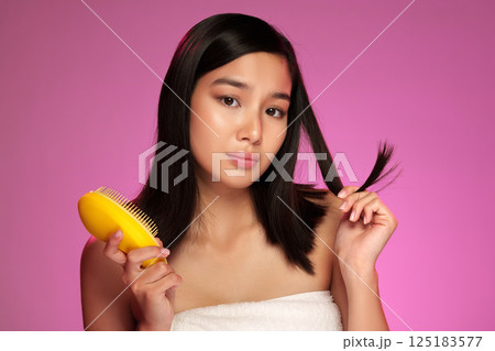 Young woman with long hair styling in front of a colored background during a beauty routine 125183577