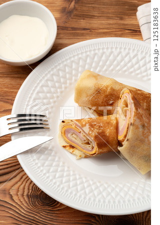 Savory crepes filled with ham and cheese served with a dollop of sour cream on a rustic wooden table 125183638