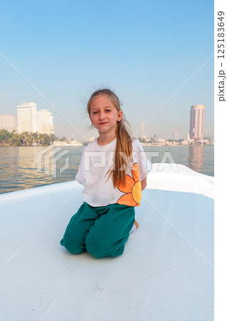 Young girl kneeling on a boat with a city skyline in the background on a clear sunny day 125183649