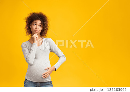 Pensive afro pregnant woman choosing name for baby on pink background 125183963