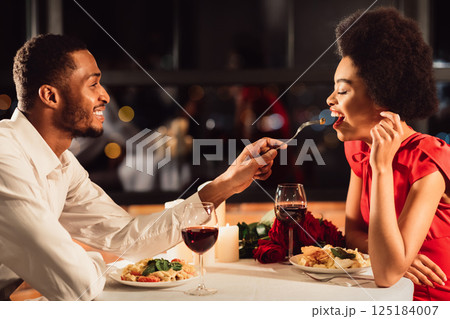 Romantic Date Concept. African American Man Feeding Girlfriend During Dinner Celebrating Anniversary In Restaurant 125184007