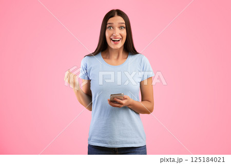 Yes. Portrait of happy surprised young woman using smartphone making winner gesture isolated over yellow studio wall background. Excited lady celebrating win, shaking clenched fist, looking at camera Yes. Portrait of happy surprised young woman using smartphone making winner gesture isolated over yellow studio wall background. Excited lady celebrating win, shaking clenched fist, looking at camera 125184021