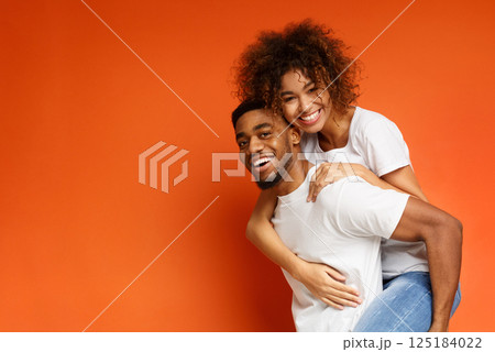 Love is so much fun. Happy african-american man and woman riding piggyback, orange background, free space Love is so much fun. Happy african-american man and woman riding piggyback, orange background, free space 125184022