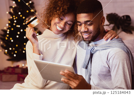 Christmas holiday. African-american couple choosing gifts on tablet, using credit card Christmas holiday. African-american couple choosing gifts on tablet, using credit card 125184043