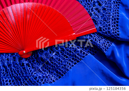 Red fan on blue lace fabric. Vibrant contrast of color and texture 125184356