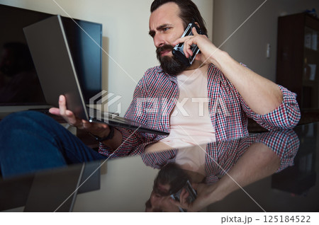 Young Man Multitasking with Laptop and Smartphone at Home Office 125184522
