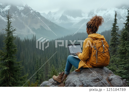 Woman during hike sitting on a rock with a laptop on her lap. Remote work. The hiker showcases the modern work-life balance, using her laptop on a rock surrounded by nature. 125184789